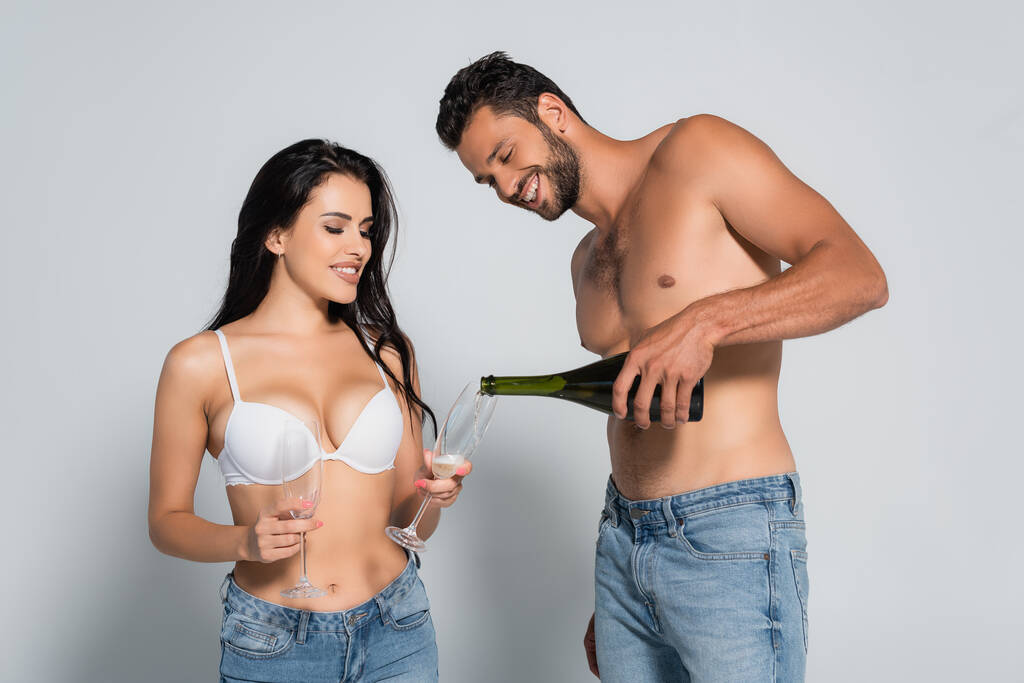 bez koszulki mężczyzna wlewanie szampana w szkło w pobliżu sexy kobieta w biustonosz na szary - Zdjęcie, obraz