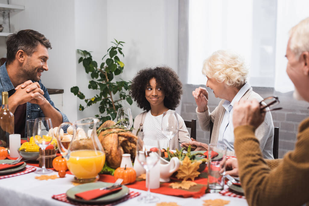 selective focus of senior woman talking to african american granddaughter during thanksgiving dinner - Photo, Image