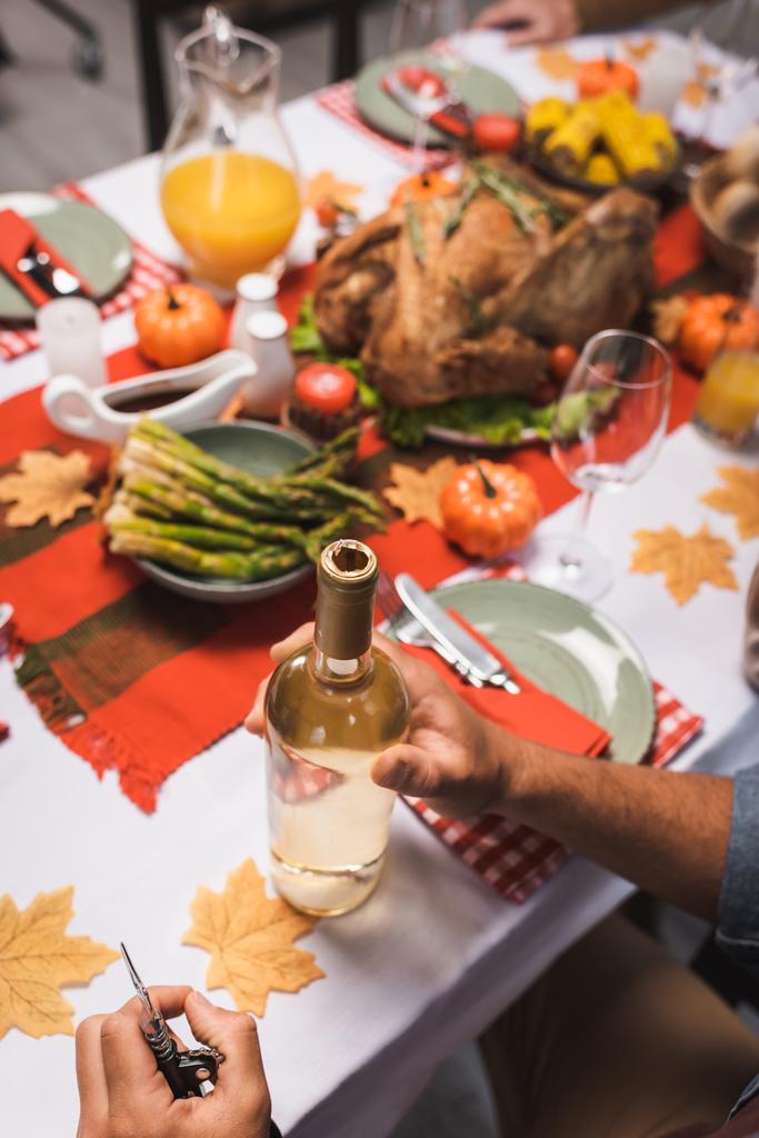 abgeschnittene Ansicht eines Mannes in der Nähe einer Flasche Weißwein am Tisch, serviert mit Danksagungsdinner - Foto, Bild
