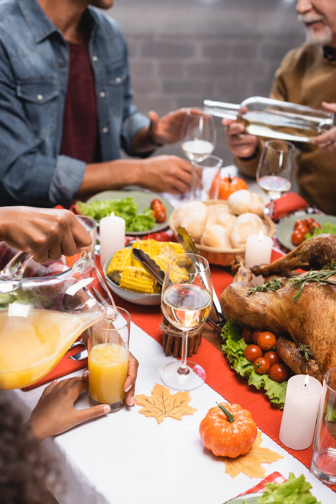 bijgesneden zicht op senior man en Afrikaans-Amerikaanse vrouw gieten witte wijn en sinaasappelsap tijdens thanksgiving diner  - Foto, afbeelding