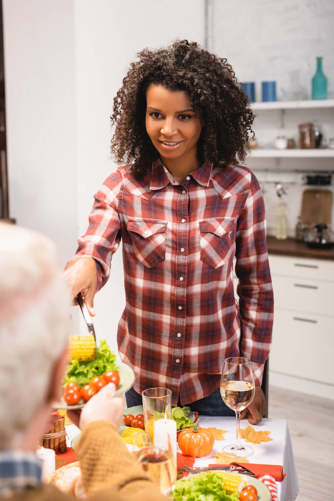senior man holding plate with vegetables near african american woman during thanksgiving dinner - Photo, Image