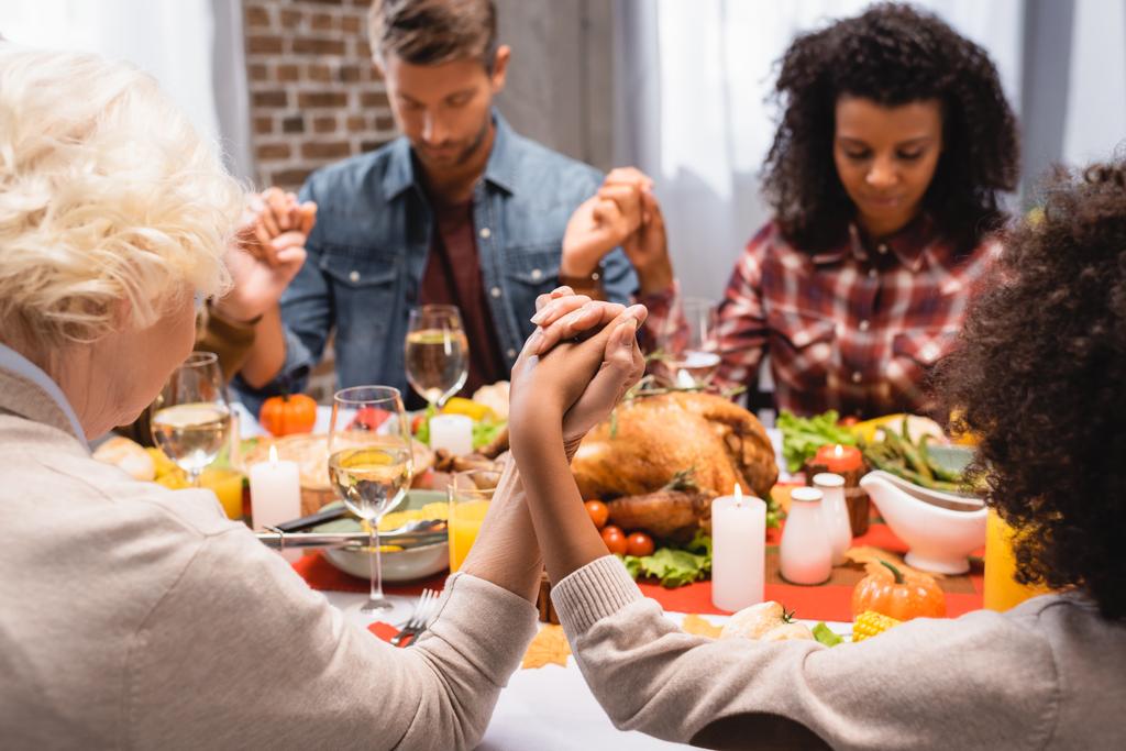 selectieve focus van multi-etnische familie met gesloten ogen hand in hand op Thanksgiving vakantie - Foto, afbeelding