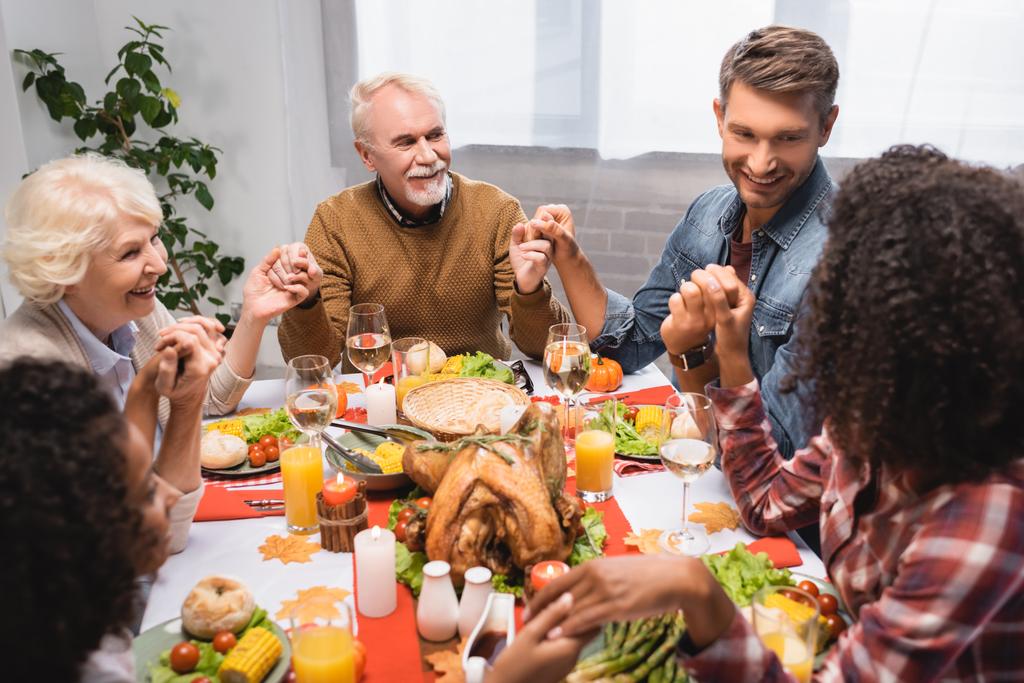 gioiosa famiglia multietnica che si tiene per mano durante la cena durante la festa del Ringraziamento - Foto, immagini