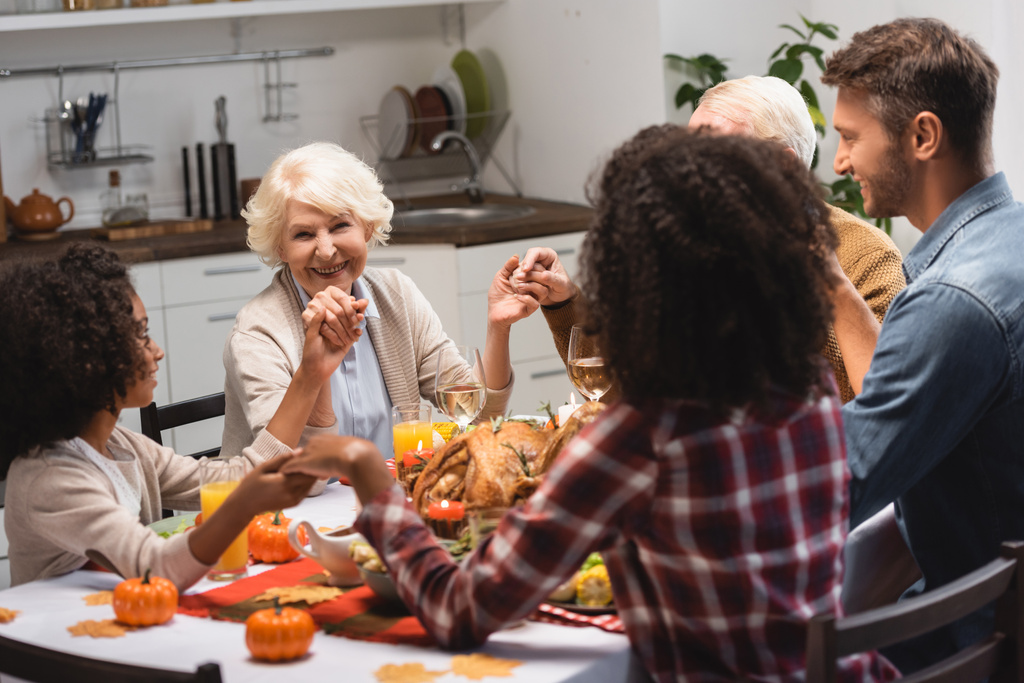 selectieve focus van vreugdevolle multiculturele familie hand in hand tijdens het diner op Thanksgiving vakantie - Foto, afbeelding