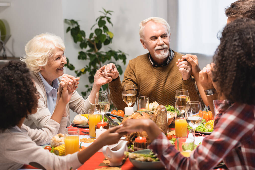 Famiglia multietnica che si tiene per mano vicino a cena durante la festa del Ringraziamento - Foto, immagini