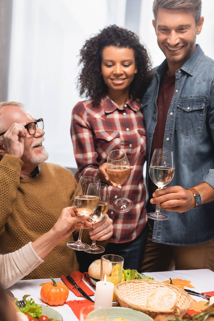 selektivní zaměření radostné multikulturní rodiny cinkání skleniček na víno během večeře na Díkůvzdání - Fotografie, Obrázek