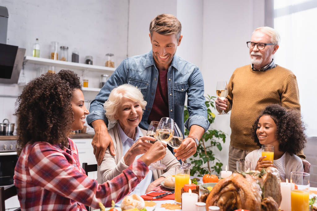 vzrušená multietnická rodina cinkání sklenice na víno během večeře na Díkůvzdání - Fotografie, Obrázek