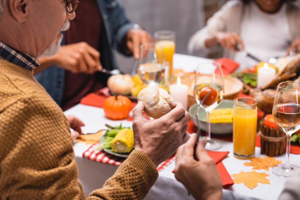 Enfoque selectivo del hombre mayor sosteniendo pan durante la cena de acción de gracias con la familia en casa   - Foto, imagen
