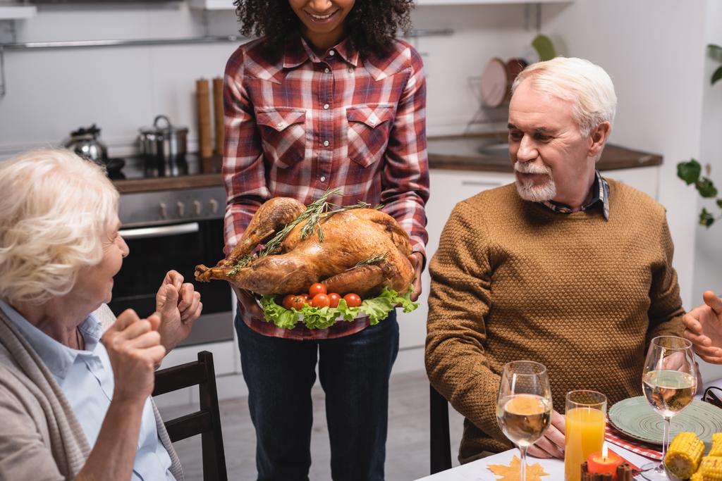 Selective focus of african american woman holding turkey near multiethnic family in kitchen  - Photo, Image