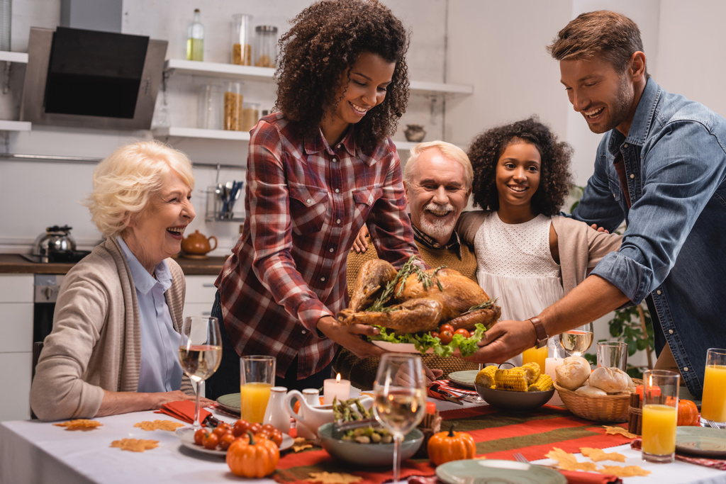 Focus selettivo della famiglia multietnica in piedi vicino al tacchino e cena del Ringraziamento a casa  - Foto, immagini
