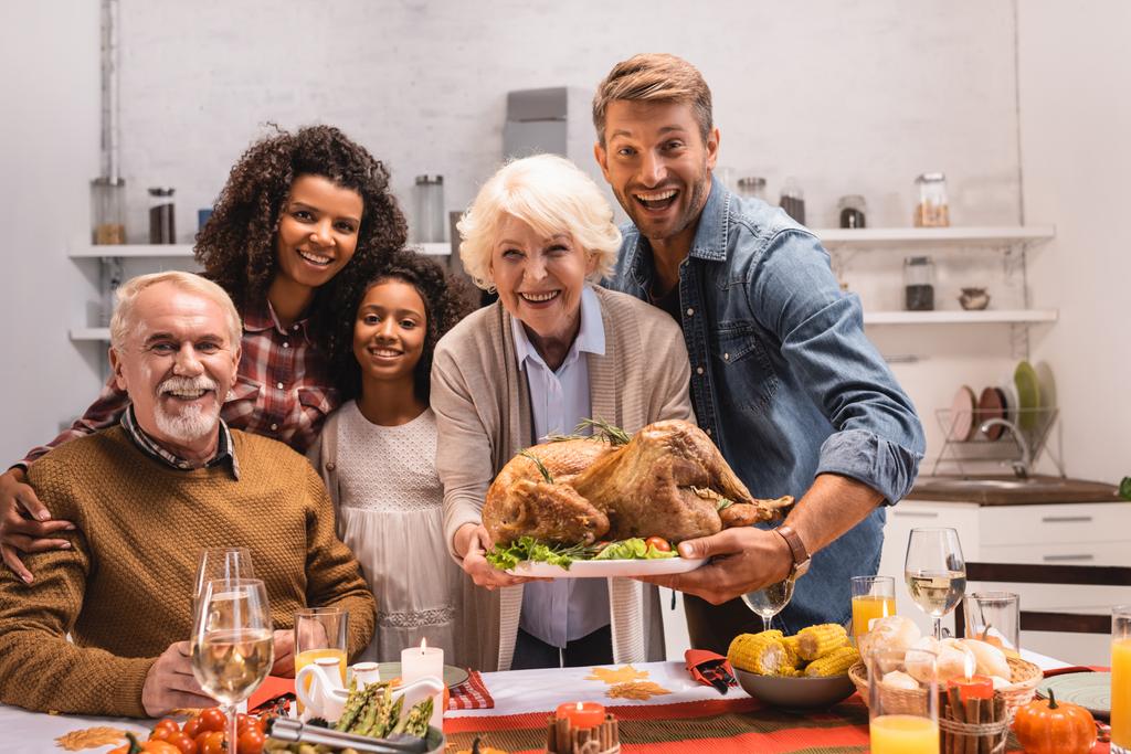 Enfoque selectivo de la familia multiétnica sosteniendo pavo y mirando a la cámara durante el Día de Acción de Gracias  - Foto, imagen
