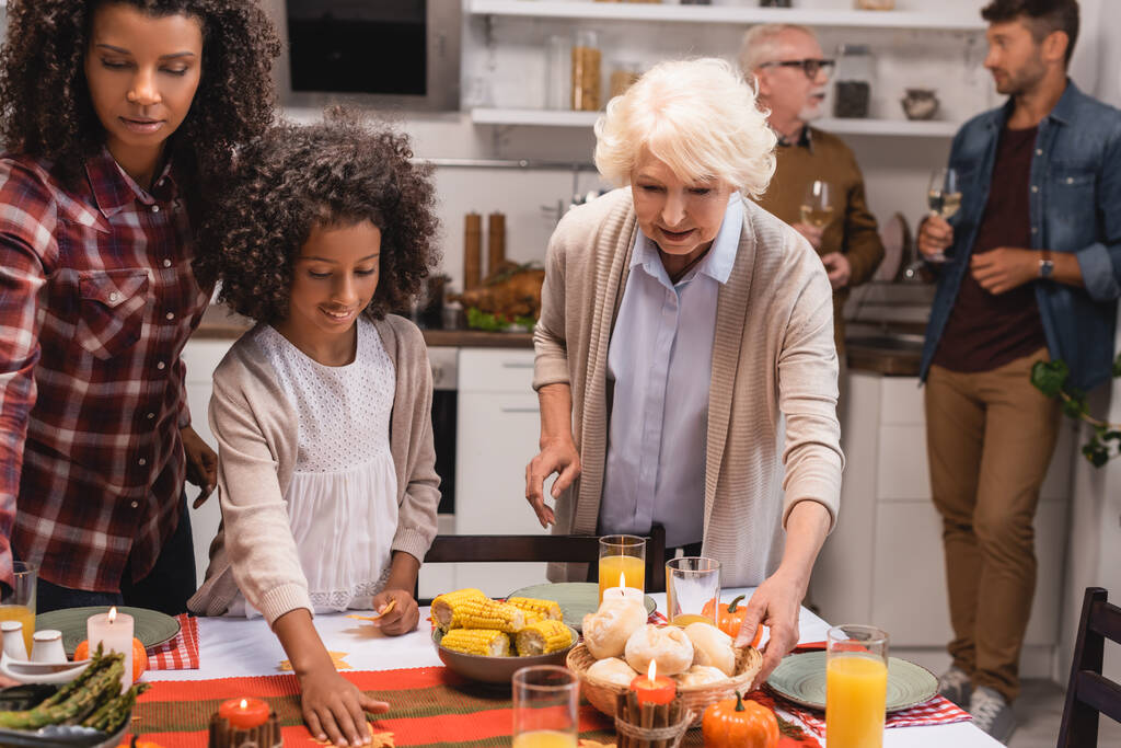 Concentration sélective de la fille afro-américaine debout près de la mère et de la grand-mère servant le dîner de Thanksgiving  - Photo, image