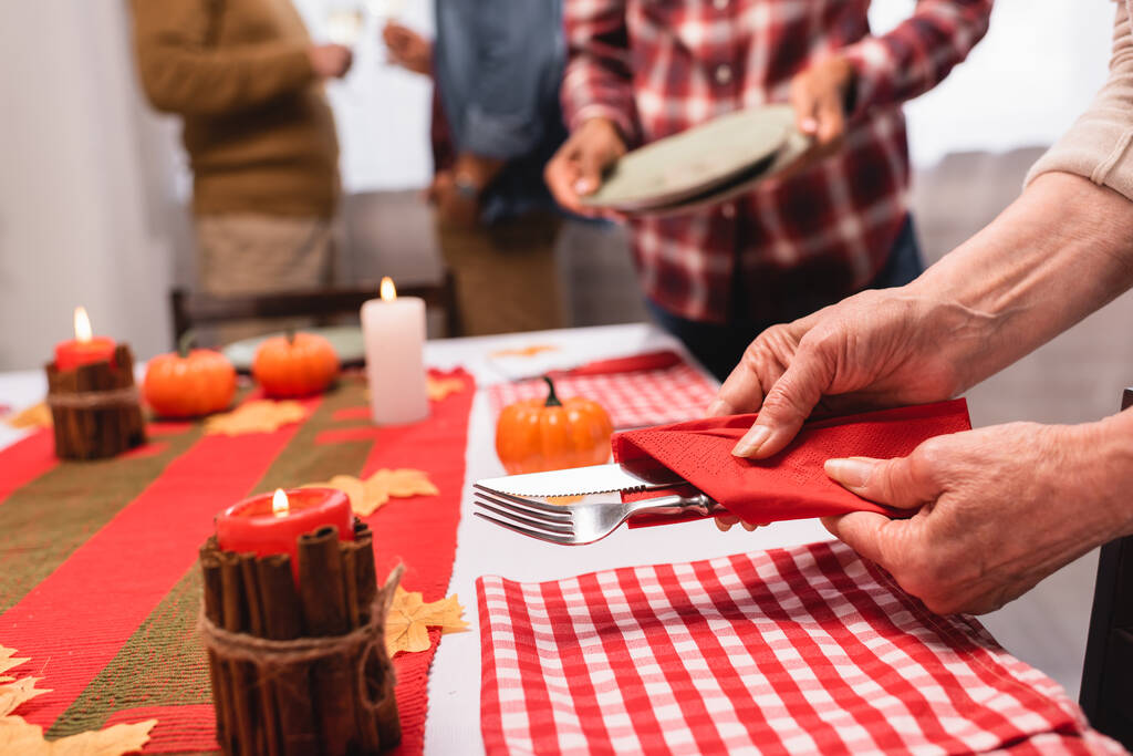 Cropped view of elderly woman holding cutlery near candles and pumpkins on table during thanksgiving  - Photo, Image