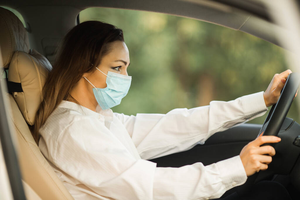hermosa mujer joven en máscara médica conducir un coche - Foto, Imagen