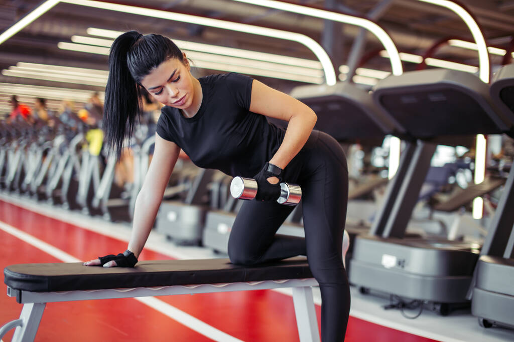 mulher flexionando músculos com haltere no banco no ginásio - Foto, Imagem