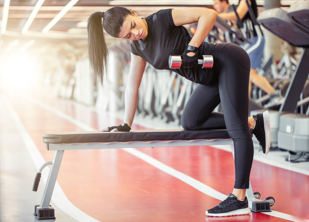 vrouw flexing spieren met halter op bank in de sportschool - Foto, afbeelding