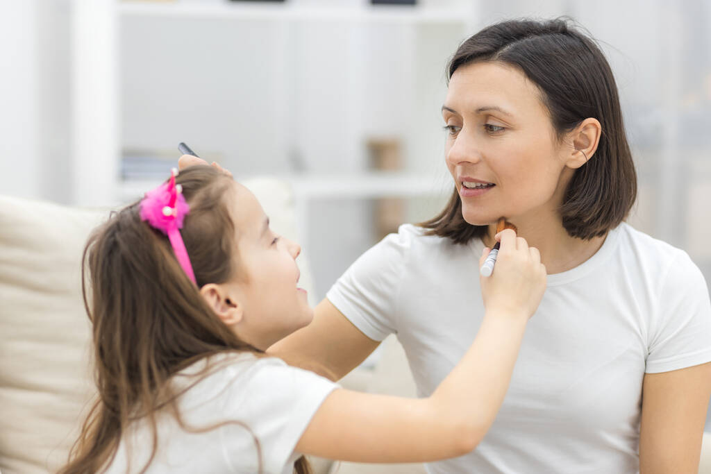 Linda madre enseñando a su hija haciendo maquillaje en casa. - Foto, imagen