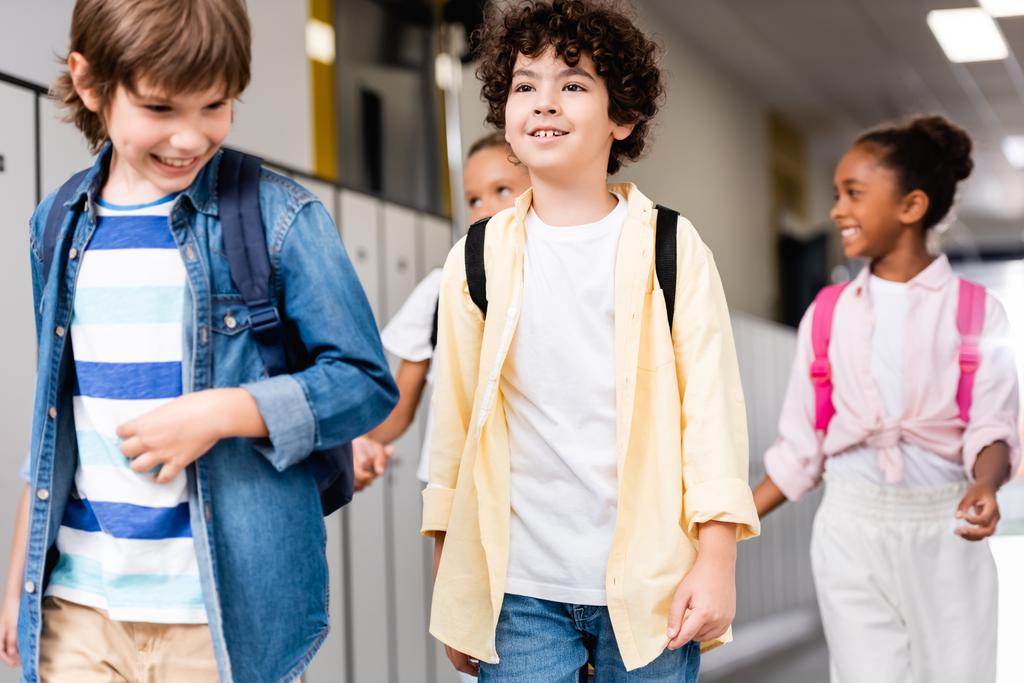 izgatott multikulturális iskolások sétálnak végig az iskolai folyosón - Fotó, kép