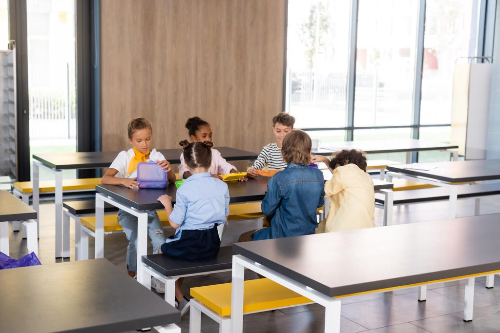 wielokulturowi uczniowie siedzący w szkolnej stołówce podczas hamulca obiadowego - Zdjęcie, obraz