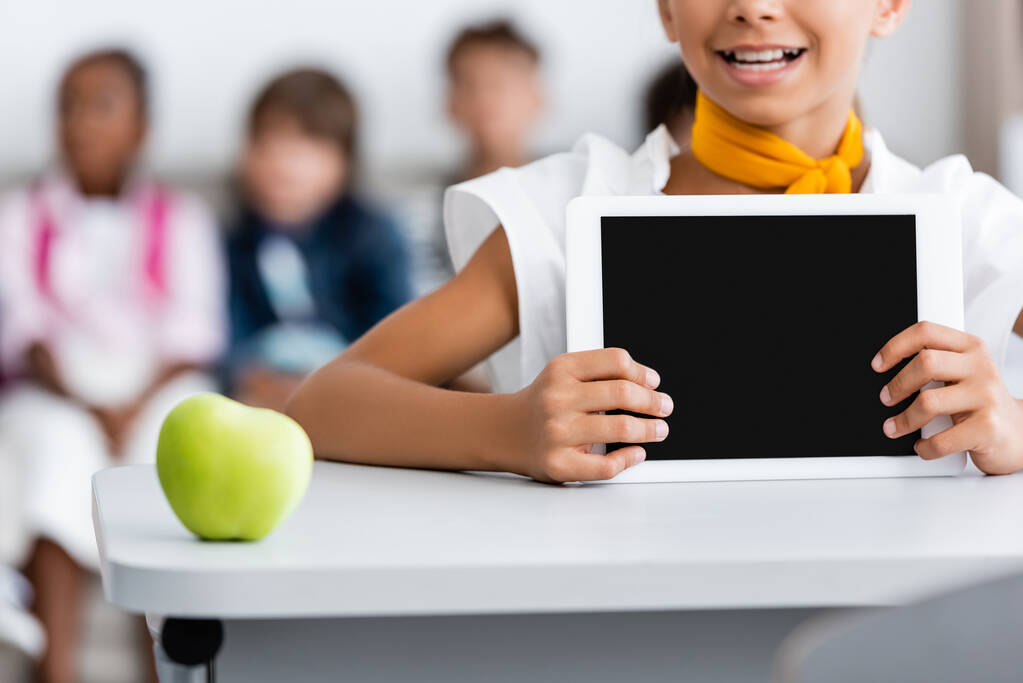 Gesneden weergave van schoolmeisje met digitale tablet met leeg scherm in de buurt van appel op het bureau  - Foto, afbeelding