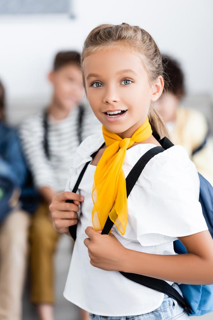 Sırt çantalı bir kızın sınıftaki kameraya baktığı seçici odak noktası.  - Fotoğraf, Görsel
