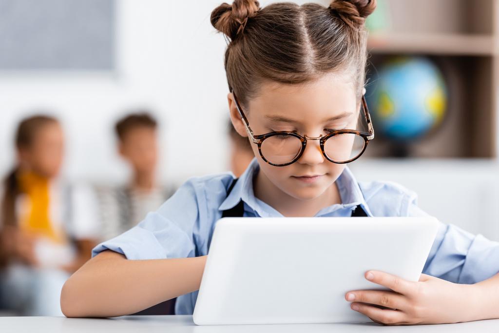 Selectieve focus van schoolmeisje in bril met digitale tablet op school  - Foto, afbeelding
