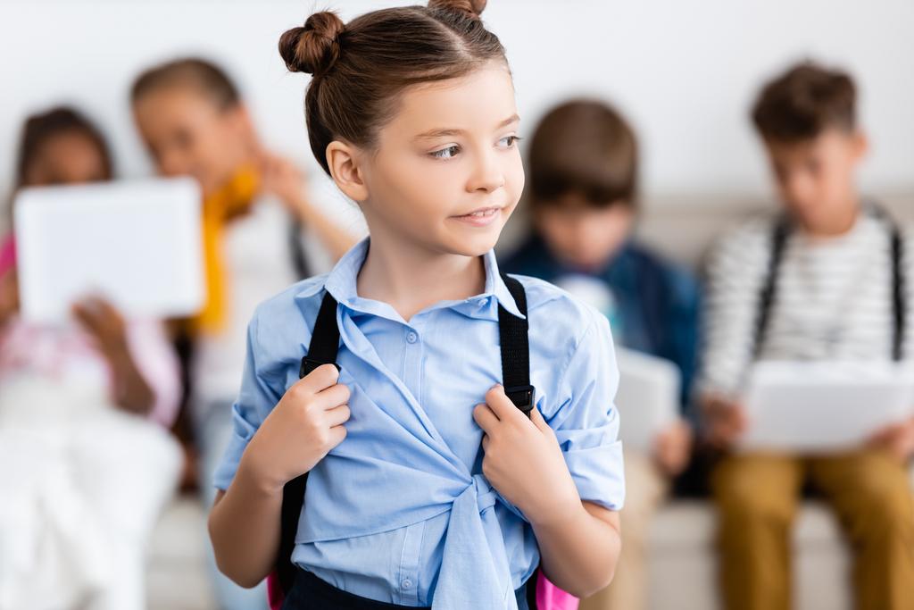 Selective focus of schoolgirl holding backpack near multiethnic friends at background  - Photo, Image