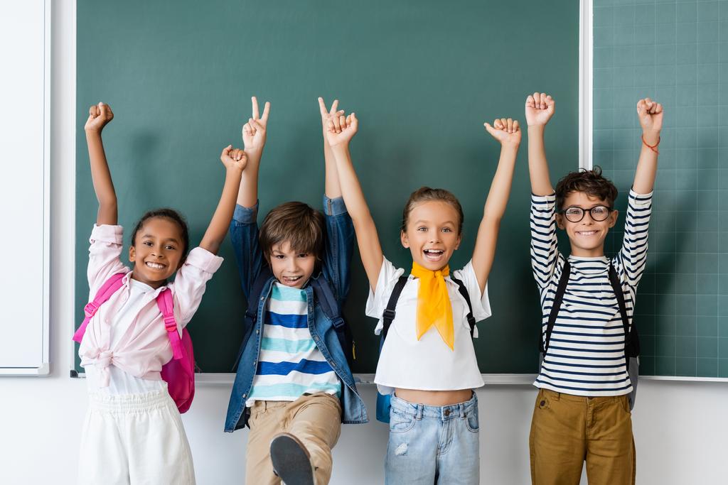 Selectieve focus van multiculturele klasgenoten die vrede tonen en ja gebaren in de buurt van schoolbord in de klas  - Foto, afbeelding