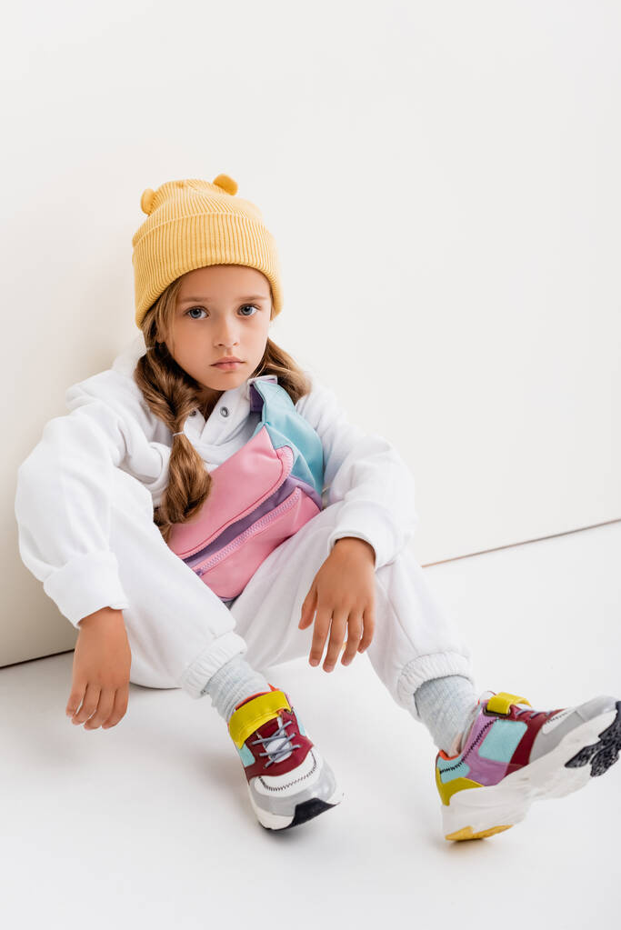 chica rubia en ropa deportiva sentado cerca de la pared blanca - Foto, Imagen