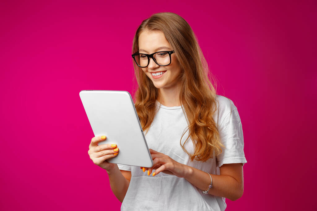Aantrekkelijke jonge vrouw met behulp van digitale tablet tegen roze achtergrond - Foto, afbeelding