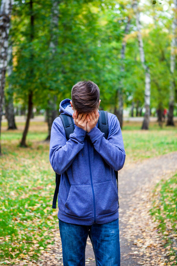 Droevige jongeman verbergt zijn gezicht en huilt in het Herfst Park - Foto, afbeelding