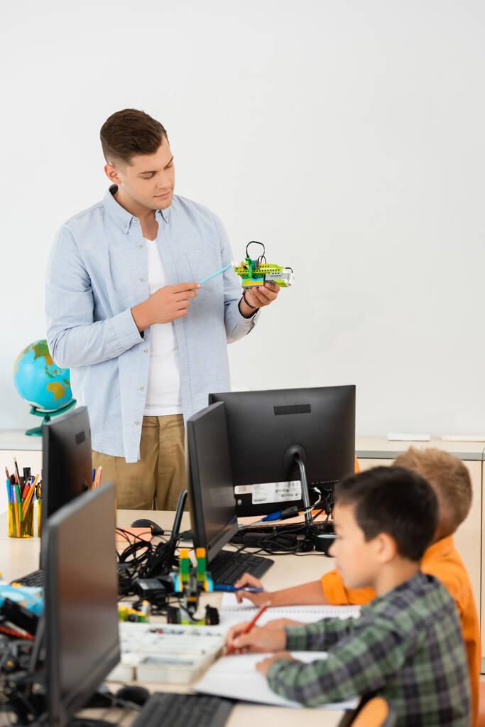 Valikoiva painopiste opettajan osoittaa robotti lähellä monikansallisten koululaisten ja tietokoneiden  - Valokuva, kuva