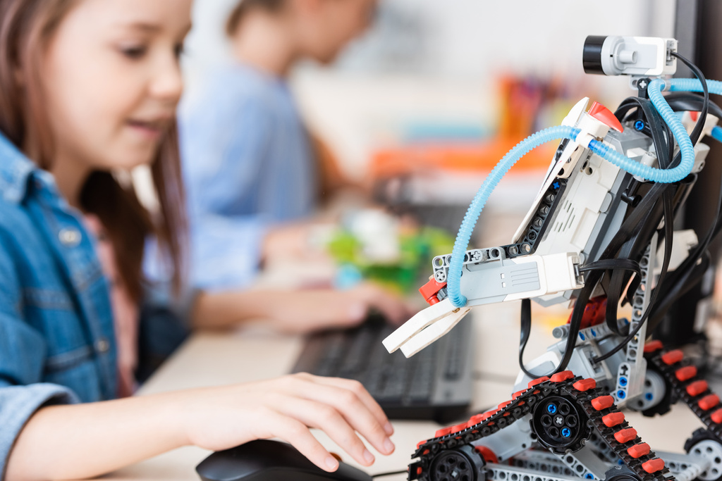Селективный фокус робота возле школьницы с помощью компьютера в школе  - Фото, изображение