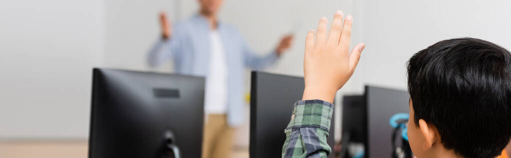 Kök okulunda bilgisayarların yanında el kaldırmış Asyalı bir öğrencinin yatay mahsulü.  - Fotoğraf, Görsel