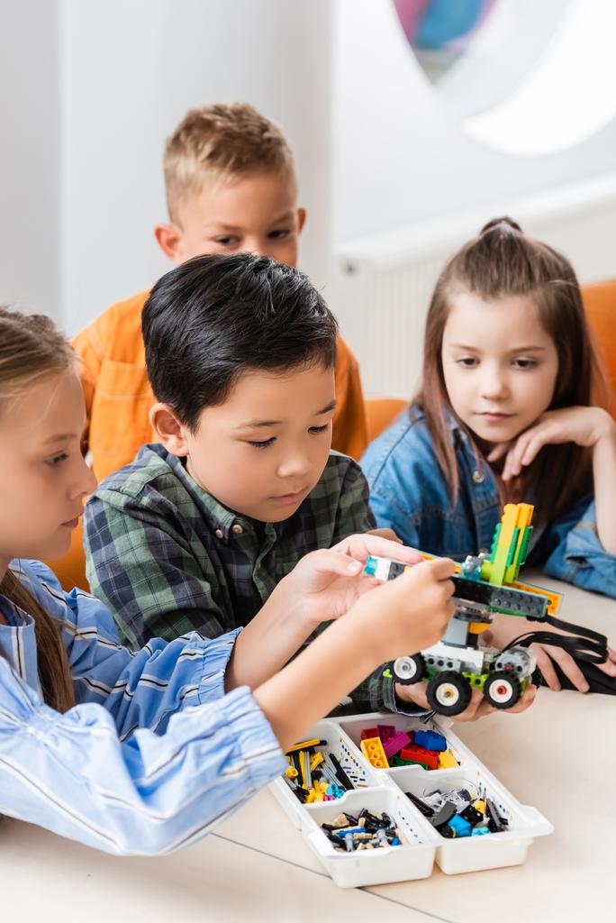 Selective focus of multiethnic kids with building blocks modeling robot in stem school   - Photo, Image