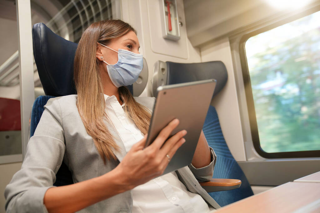 Empresaria viajando en tren, trabajando en tableta digital y usando mascarilla facial - Foto, imagen