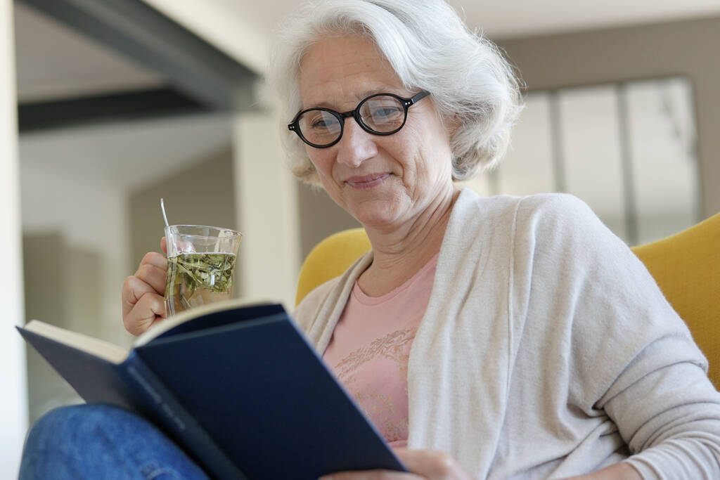 Idős nő pihentető karosszékben és olvasókönyv - Fotó, kép
