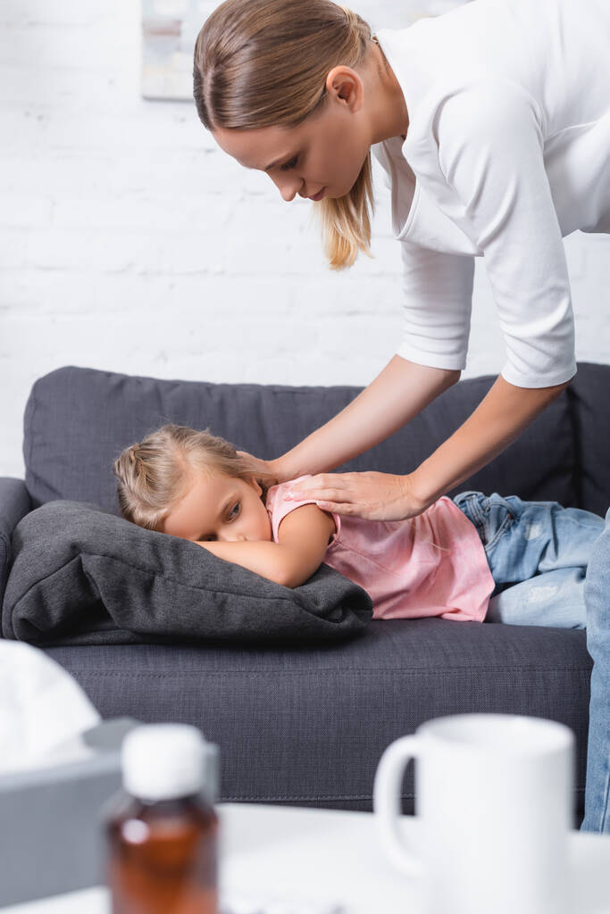 Valikoiva painopiste nuori nainen koskettaa sairaan lapsen lähellä cup ja lautasliinat sohvapöytä  - Valokuva, kuva