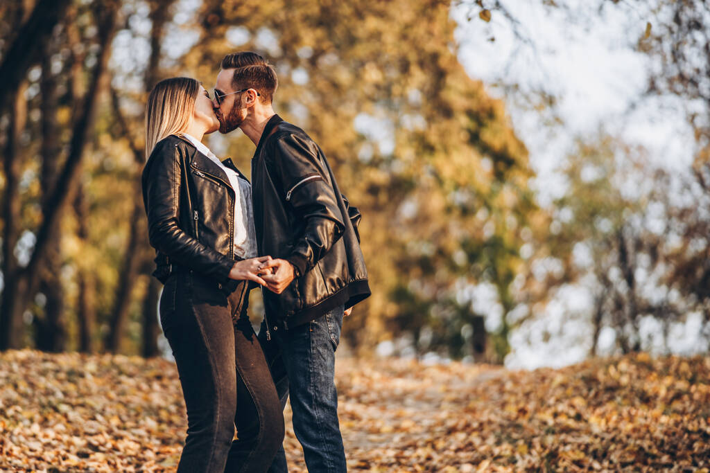 Hermosa pareja joven caminando en el parque de otoño en un día soleado. Se abrazan y sonríen, disfrutan de un paseo
. - Foto, imagen