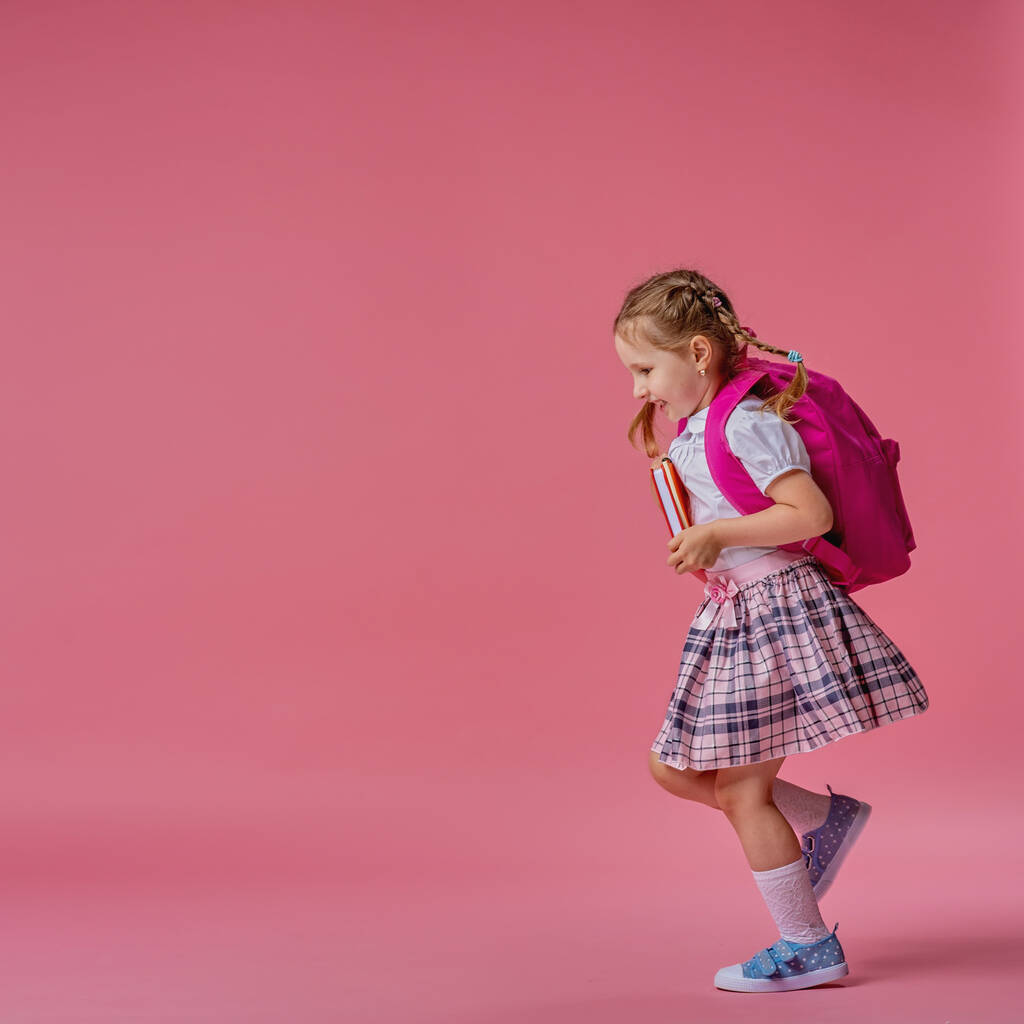 Πίσω στο σχολείο! Χαριτωμένο εργατικό παιδί με στολή, κάνει τζόγκινγκ σε ροζ φόντο. Παιδί με σακίδιο. Το κοριτσάκι είναι έτοιμο για το σχολείο. Δυναμικές εικόνες που πηγαίνουν πίσω στο εννοιολογικό σχολείο. έναρξη διακοπών. - Φωτογραφία, εικόνα