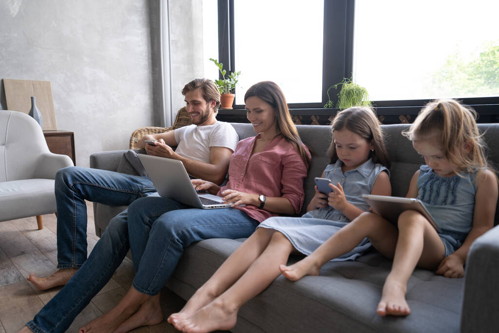Nykyaikaiset perhearvot. Isä, äiti ja tyttäret käyttävät elektronisia laitteita - Valokuva, kuva