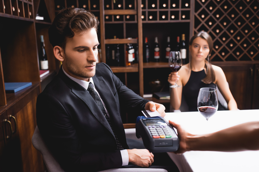 Enfoque selectivo del hombre con tarjeta de crédito que paga a la camarera con terminal de pago durante las citas con su novia en el restaurante  - Foto, imagen