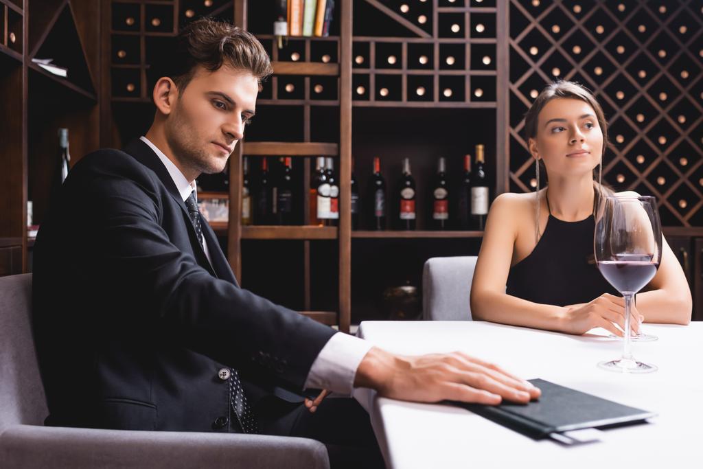 Selectieve focus van de man zetten restaurant rekening met creditcard op tafel in de buurt van vriendin met glas wijn  - Foto, afbeelding