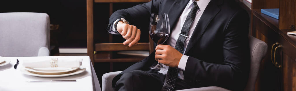 Website header of man in suit holding glass of wine and checking time in restaurant  - Photo, Image