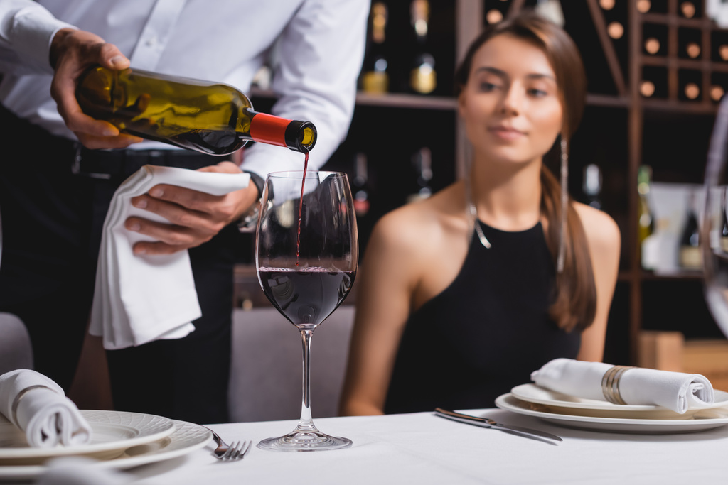Selektywne skupienie sommelier nalewanie wina w pobliżu kobiety przy stole w restauracji  - Zdjęcie, obraz