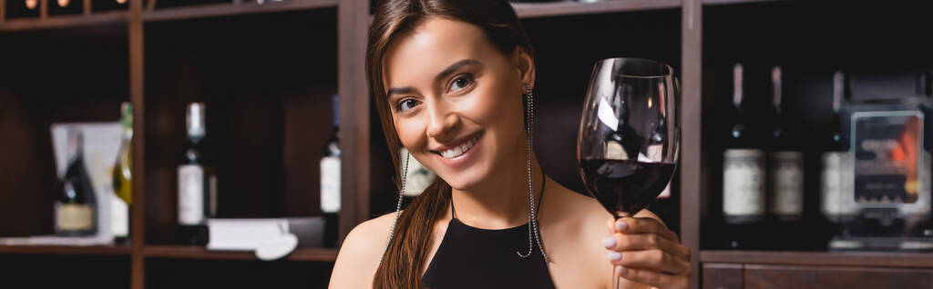 Panoraamakuva nuoresta naisesta pitelemässä viinilasia ja katselemassa kameraa ravintolassa  - Valokuva, kuva