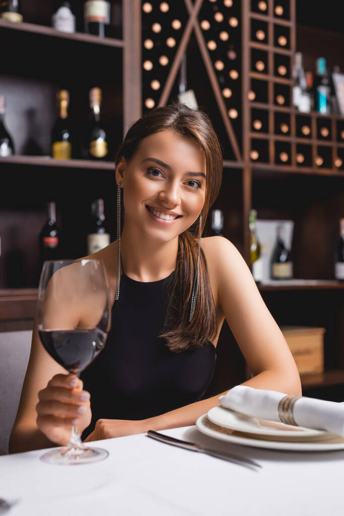 Вибірковий фокус молодої жінки з келихом вина дивиться на камеру n ресторану
  - Фото, зображення