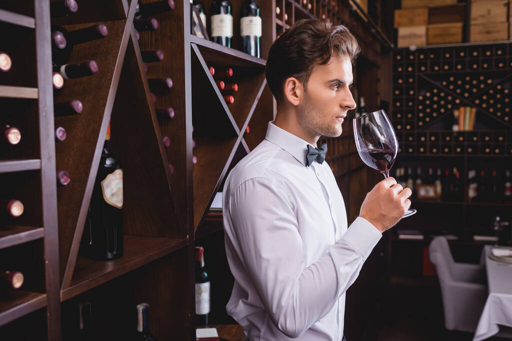 Επιλεκτική εστίαση του νεαρού σομελιέ μυρίζοντας κρασί σε ποτήρι ενώ εργάζεται στο εστιατόριο  - Φωτογραφία, εικόνα
