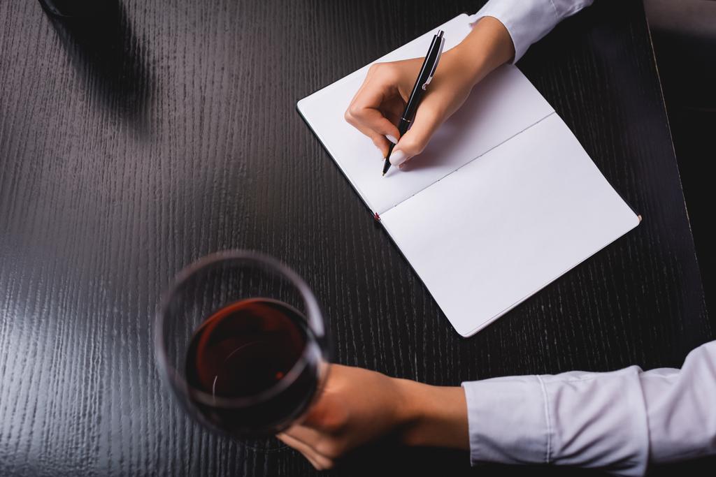 Vágott kilátás sommelier írás notebook, miközben egy pohár bort az asztalnál - Fotó, kép