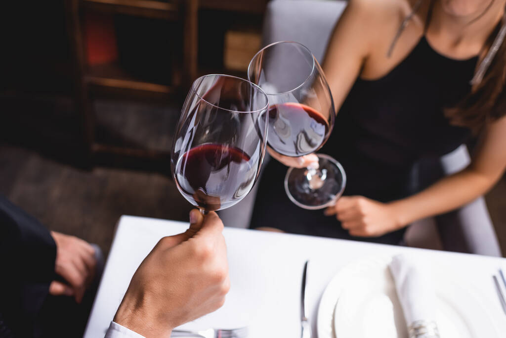 Обрезанный вид молодой пары звон с классами вина в ресторане  - Фото, изображение